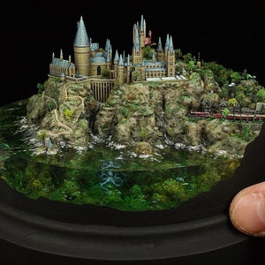 May include: A detailed miniature model of Hogwarts castle, perched on a rocky island with a surrounding body of water. The castle is made of stone and has many towers and windows. The water is clear and you can see the bottom of the lake, where there is a small octopus.