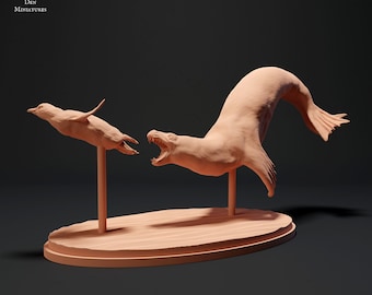 May include: A miniature figurine of a seal leaping out of the water, with its mouth open, and a miniature figurine of a penguin flying in the air. Both figurines are painted in a light brown colour and are mounted on a light brown oval base.