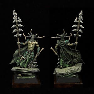 May include: A green and brown painted miniature figurine of a horned, cloaked figure holding a spear with a bone handle. The figure is standing on a rocky base.