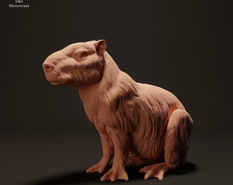 May include: A light brown capybara figurine in a seated pose. The figurine has detailed fur texture and is set against a dark background. The text "ANIMAL DEN MINIATURES" is in the upper left corner.