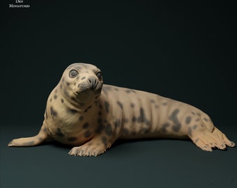 May include: A grey and brown spotted seal figurine lying on its belly with its head turned to the side. The seal has a light brown nose and black eyes.