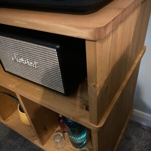 以下が含まれることがあります： 黒いMarshallスピーカーを備えた、明るい茶色の木製棚。スピーカーは銀色のメッシュフロントとMarshallのロゴが付いています。このユニットには複数の収納スペースがあり、明るい色の木材で作られています。