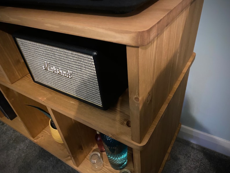 以下が含まれることがあります： 黒いMarshallスピーカーを備えた、明るい茶色の木製棚。スピーカーは銀色のメッシュフロントとMarshallのロゴが付いています。このユニットには複数の収納スペースがあり、明るい色の木材で作られています。