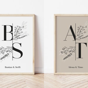 Könnte beinhalten: Zwei gerahmte Drucke mit schwarzen und weißen Blumenmustern und den Initialen "BS" und "AT" mit den Namen "Bastian & Steffi" und "Alessa & Timo" darunter.