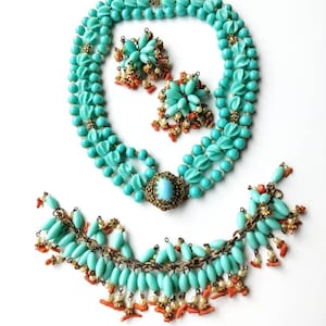 May include: A vintage jewelry set featuring a turquoise beaded necklace and matching earrings. The necklace has multiple strands and a central pendant. The earrings and necklace are accented with coral and gold-tone details. The set is displayed on a white background.