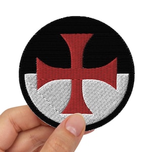 May include: A round embroidered patch with a red cross on a white background. The patch is surrounded by a black border.