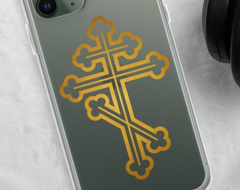 May include: A green phone case with a gold geometric cross design. The case is on a white fluffy surface next to black headphones.