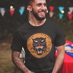 May include: A black t-shirt with a vintage-style graphic of a black panther with a tank in its mouth. The graphic is surrounded by a circle with the text "Seek... Strike... Destroy".