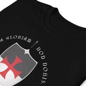 May include: Black t-shirt with a white graphic of a shield with a red cross and the text "In Gloriam Don Nobis".