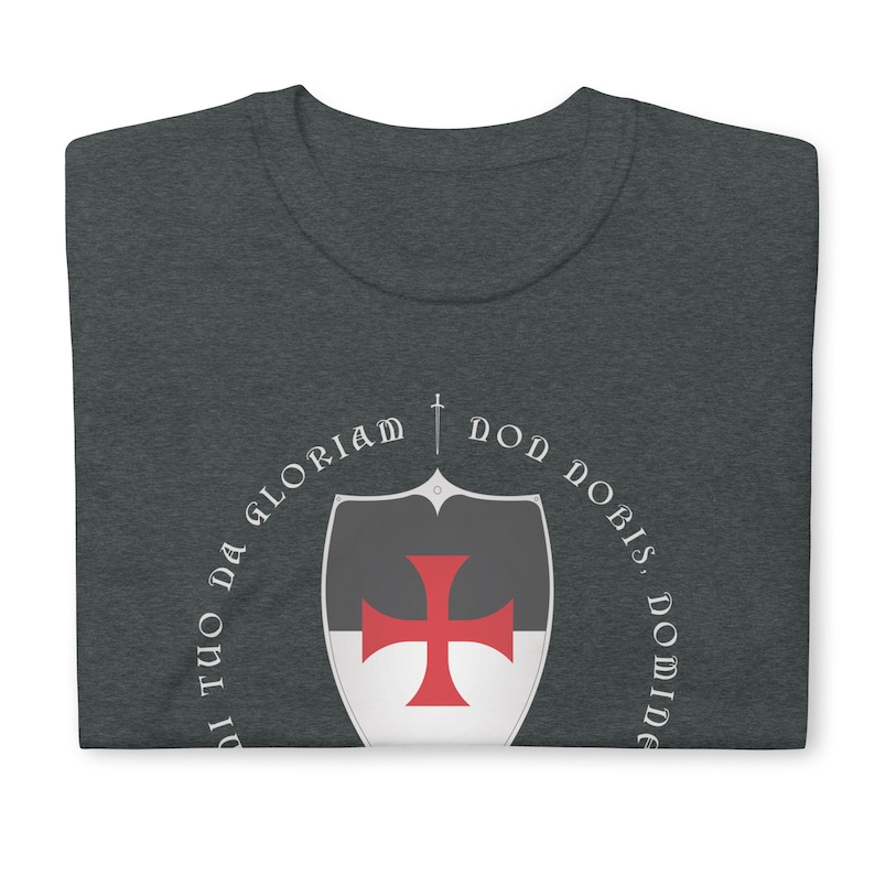 May include: A dark heather grey t-shirt with a white circle design featuring a red cross on a shield and the text "Non Nobis, Domine, Non Nobis, Sed Nomini Tuo Da Gloriam".