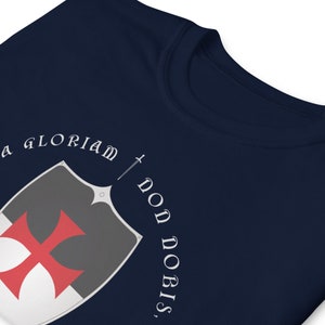 May include: Navy blue t-shirt with a white shield and red cross, and the text "In Gloriam Don Nobis".