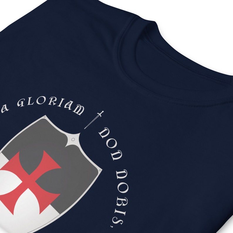 May include: Navy blue t-shirt with a white shield and red cross, and the text "In Gloriam Don Nobis".