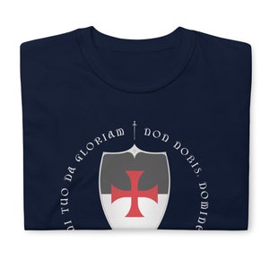 May include: A navy blue t-shirt with a white circle design featuring a sword, a shield with a red cross, and the text "Non Nobis, Domine, Sed Tuo Da Gloriam".