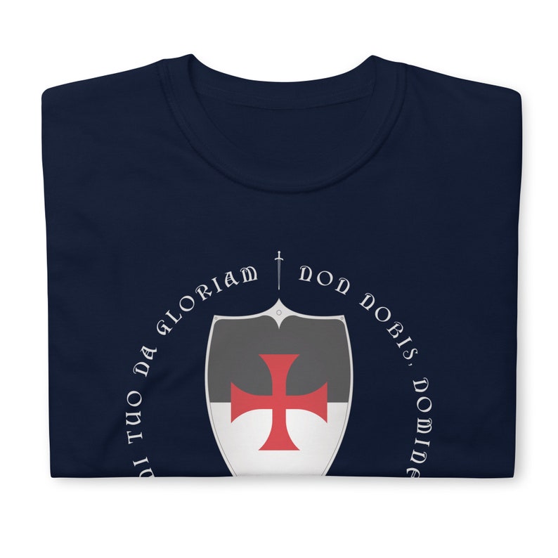 May include: A navy blue t-shirt with a white circle design featuring a sword, a shield with a red cross, and the text "Non Nobis, Domine, Sed Tuo Da Gloriam".