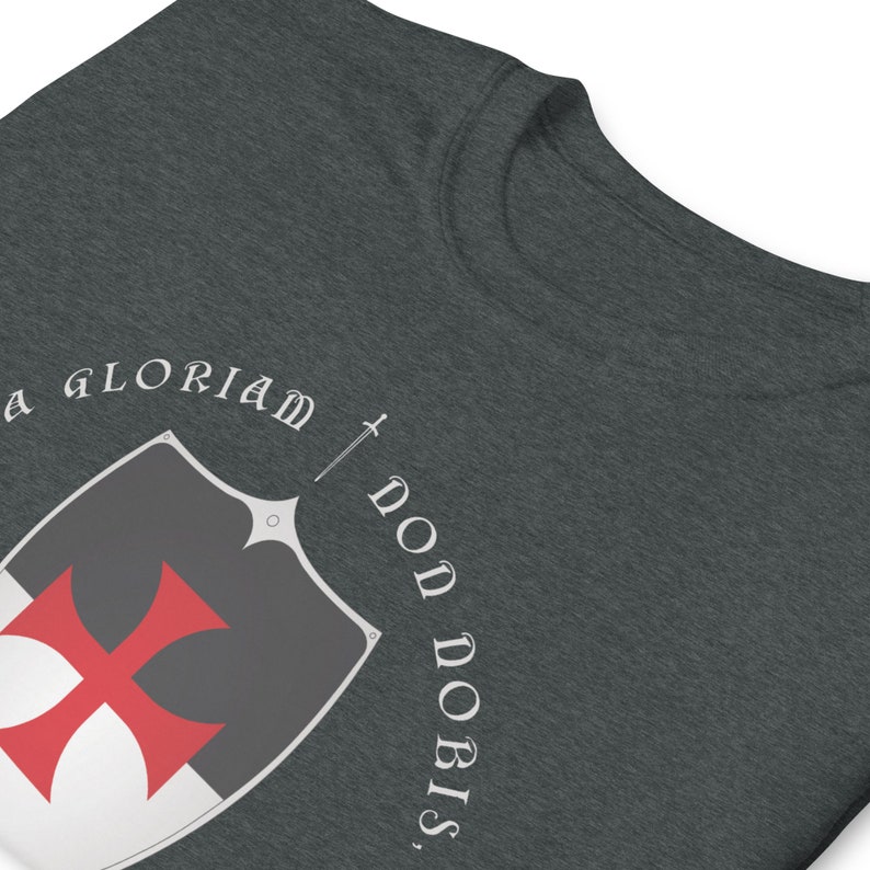 May include: A dark gray t-shirt with a white and red shield and sword design. The text "In Gloriam Dono Nobis" is printed around the shield.