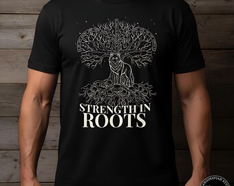 以下が含まれることがあります： 黒いTシャツ。白いグラフィックで、木の下にいるオオカミと「STRENGTH IN ROOTS」の文字が描かれています。デザインはスカンジナビア風です。Tシャツは黒色です。