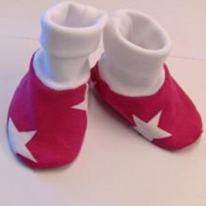 May include: A pair of baby booties. The booties are a vibrant pink with a white star on each side. The cuffs are white and folded over. The booties are made of soft fabric.