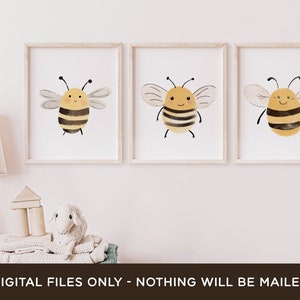 May include: Three printable art prints featuring watercolor illustrations of cute cartoon bees with yellow and black stripes. The bees have smiling faces and are set against a white background.