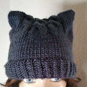Op de afbeelding: Een donkergrijze gebreide beanie met kattenoren. De beanie is gemaakt van zacht, warm garen en heeft een eenvoudig, klassiek ontwerp.