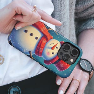 May include: A phone case featuring a whimsical snowman design. The case has a blue background with a snowman wearing a red scarf and a carrot nose. The snowman has button eyes and is set against a snowy backdrop. The case is designed for a smartphone.