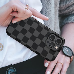 May include: A smartphone case featuring a dark gray and black checkered pattern. The case has a precise cutout for the triple-lens camera system and flash on the back. The design covers the entire rear surface of the phone case in a uniform grid.