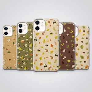 May include: Five clear smartphone cases arranged in a row, each featuring a unique pattern of autumn-themed illustrations including various colorful leaves and acorns set against different background shades of tan, olive green, and dark brown.