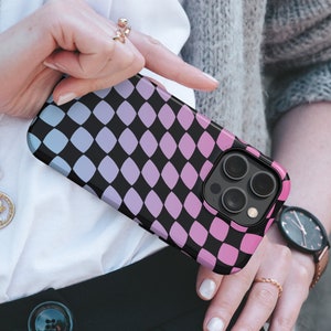 Può includere: Custodia per smartphone con un motivo geometrico nero di disegni a forma di diamante sovrapposti in tonalità di blu, viola e rosa. La custodia ha un bordo nero e un ritaglio per la fotocamera.