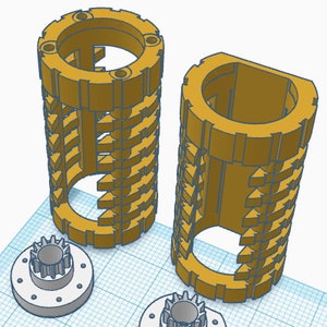 May include: Two gold-coloured 3D printed gears with a smaller gear attached to each. The gears have a cylindrical shape with a series of teeth around the circumference. The gears are on a white grid background.