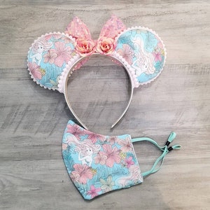 Pode incluir: Um par de orelhas de rato rosa e azul com um design floral e uma m&aacute;scara facial floral combinando.