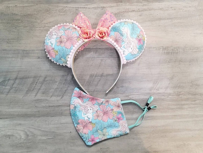 Pode incluir: Um par de orelhas de rato rosa e azul com um design floral e uma m&aacute;scara facial floral combinando.