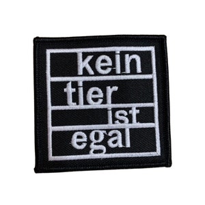 Könnte beinhalten: Schwarz-weiß gestickter Aufnäher mit dem Text "kein tier ist egal" in weißer Schrift auf schwarzem Hintergrund.