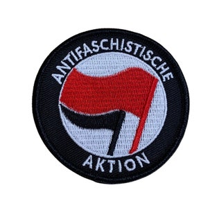 Könnte beinhalten: Ein gestickter schwarzer und weißer Aufnäher mit einer roten Flagge und dem Text "ANTIFASCHISTISCHE AKTION".