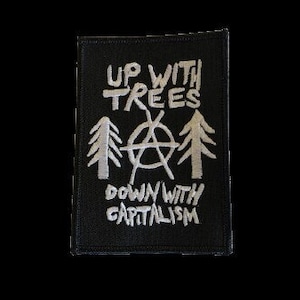 Könnte beinhalten: Schwarzer Patch mit weiß gesticktem Text, der "Up with Trees" und "Down with Capitalism" lautet. Der Text ist von drei stilisierten Bäumen und einem Anarchiesymbol umgeben.