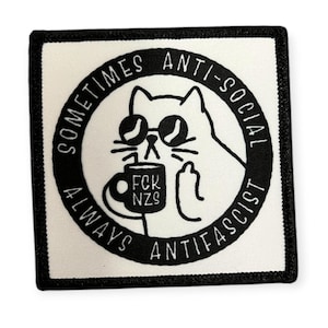 Könnte beinhalten: Quadratischer Aufnäher mit schwarzem Rand und weißer Mitte. Der Aufnäher zeigt eine schwarz-weiße Cartoon-Katze mit Sonnenbrille, die einen Becher mit der Aufschrift "FCK NZS" hält. Der Text um die Katze lautet "SOMETIMES ANTI-SOCIAL ALWAYS ANTIFASCIST."