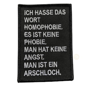 Könnte beinhalten: Schwarzer gestickter Aufnäher mit weißem Text, der "ICH HASSE DAS WORT HOMOPHOBIE. ES IST KEINE PHOBIE, MAN HAT KEINE ANGST. MAN IST EIN ARSCHLOCH." lautet.
