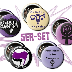 Könnte beinhalten: Satz mit fünf feministischen Anstecknadeln mit verschiedenen Designs. Die Nadeln sind in den Farben Lila, Schwarz und Weiß gehalten. Der Text auf den Nadeln lautet "My Body My Choice", "Gegen die sexistische Normalitat!", "Antissexistische Aktion" und "Feminism is for Everyone".