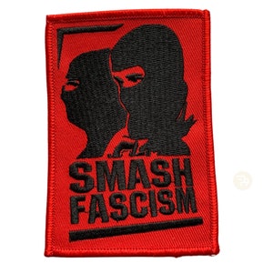 Könnte beinhalten: Roter gestickter Aufnäher mit zwei schwarzen Silhouetten von Personen, die Sturmhauben tragen. Der Text "SMASH FASCISM" befindet sich unter den Silhouetten.