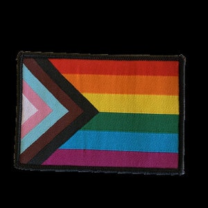 Könnte beinhalten: Ein schwarzer, brauner, rosa, hellblauer, dunkelblauer, grüner, gelber, orangefarbener und roter Stolz-Flaggen-Patch mit schwarzem Rand.