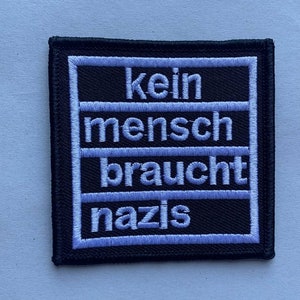 Könnte beinhalten: Schwarzer gestickter Aufnäher mit weißem Text, der "kein mensch braucht nazis" lautet.
