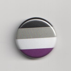 Könnte beinhalten: Ein runder Knopf mit einem schwarz-grau-weiß-violetten Streifenmuster. Der Knopf ist eine Darstellung der asexuellen Pride-Flagge.