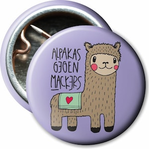 Könnte beinhalten: Ein runder, hellvioletter Knopf mit einer Cartoon-Alpaka-Illustration. Das Alpaka ist braun mit einer grünen Decke und einem roten Herzen. Der Text "ALPAKAS GJOEN MACKERS" ist in Schwarz geschrieben.