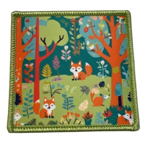Könnte beinhalten: Ein grüner, orangefarbener und blauer Stoff-Patch mit einem sich wiederholenden Muster von Füchsen in einem Wald. Der Patch hat einen grünen Rand.