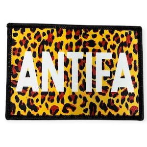 Könnte beinhalten: Rechteckiger Aufnäher mit gelbem Leopardenmuster und dem Wort "ANTIF" in weißen Großbuchstaben. Der Aufnäher hat einen schwarzen Rand.
