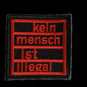 Könnte beinhalten: Ein schwarzer und roter gestickter Aufnäher mit dem Text "kein mensch ist illegal" in rot.