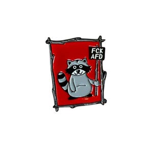 Könnte beinhalten: Eine rote Emaille-Anstecknadel mit einem Cartoon-Waschbären, der ein Schild mit der Aufschrift "FCK AFD" hält. Der Waschbär trägt eine schwarze Augenmaske und hat einen weißen Bauch. Die Anstecknadel ist von einem schwarzen Metallrahmen umgeben.