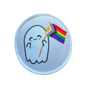 Könnte beinhalten: Ein weißer gestickter Aufnäher mit einem Cartoon-Geist, der eine Regenbogen-Pride-Flagge hält. Der Geist hat ein fröhliches Gesicht und hält die Flagge mit seiner rechten Hand.