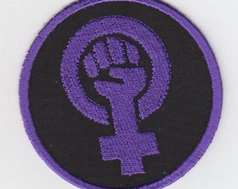 May include: Purple embroidered patch with a raised fist inside a female symbol on a black background.