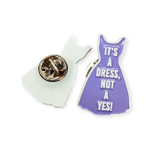 Könnte beinhalten: Zwei kleidförmige Emaille-Anstecknadeln. Eine ist weiß, die andere ist lila mit dem Text "IT'S A DRESS, NOT A YES!". Beide Anstecknadeln haben einen goldfarbenen Nadelrücken.