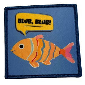 Könnte beinhalten: Ein blauer und gelber gestickter Aufnäher mit einem Cartoon-Fisch und einer Sprechblase, auf der "BLUB, BLUB!" steht.
