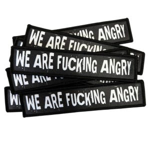 Könnte beinhalten: Ein Stapel rechteckiger schwarzer Stoffaufnäher mit weißem gesticktem Text, der WE ARE FUCKING ANGRY lautet. Die Aufnäher haben eine fette serifenlose Schrift mit abgenutzter Optik und einen dicken, schwarz umkettelten Rand.